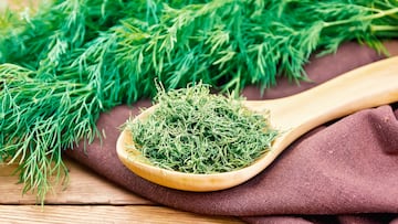 Dry dill in a spoon on a napkin, fresh herb on the background of an old wooden board
